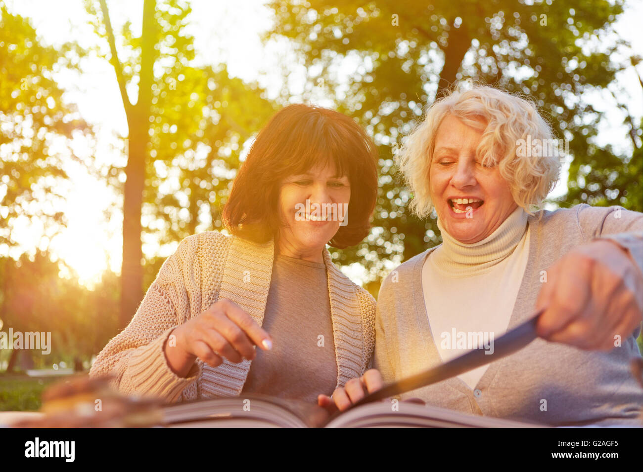 Zwei alte Frauen lesen Rezepte zusammen in einem Buch in einem Garten Stockfoto