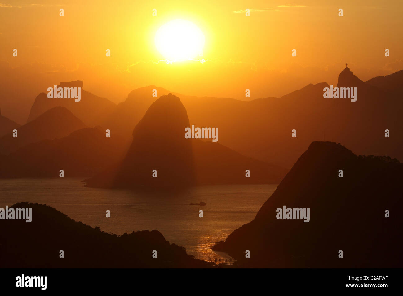 Übersicht über die Berge von Rio De Janeiro und Eingang der Guanabara-Bucht bei Sonnenuntergang mit Zuckerhut in der Mitte, Pedra da Gavea (Rock Gavea) auf der linken Seite - Hintergrund und Corcovado Berg mit Christus der Erlöser Statue auf davon auf der rechten Seite, Brasilien. Stockfoto