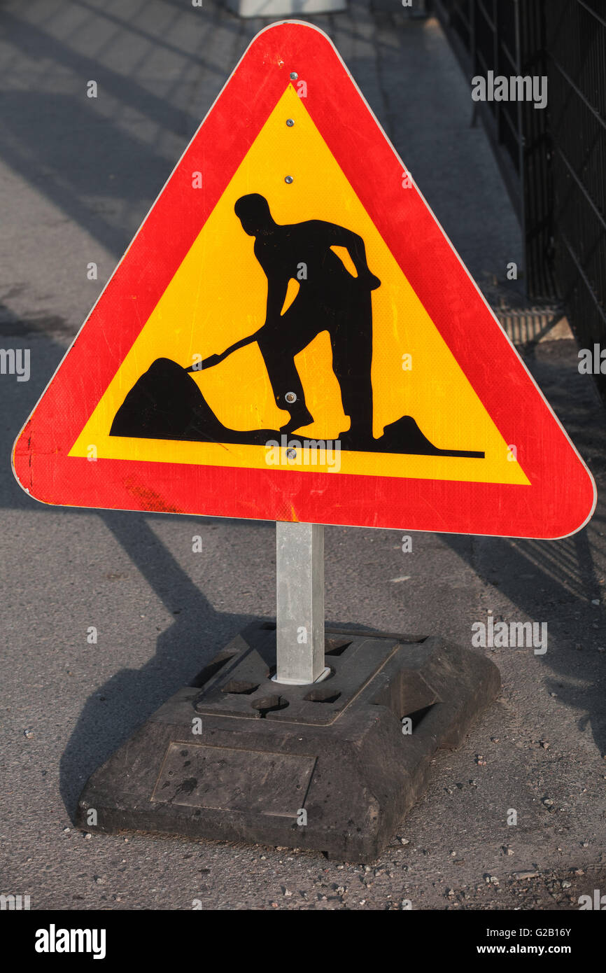 Dreieck rot und gelb Straßenschild steht am Straßenrand. Männer bei der Arbeit, Straße im Bau Stockfoto