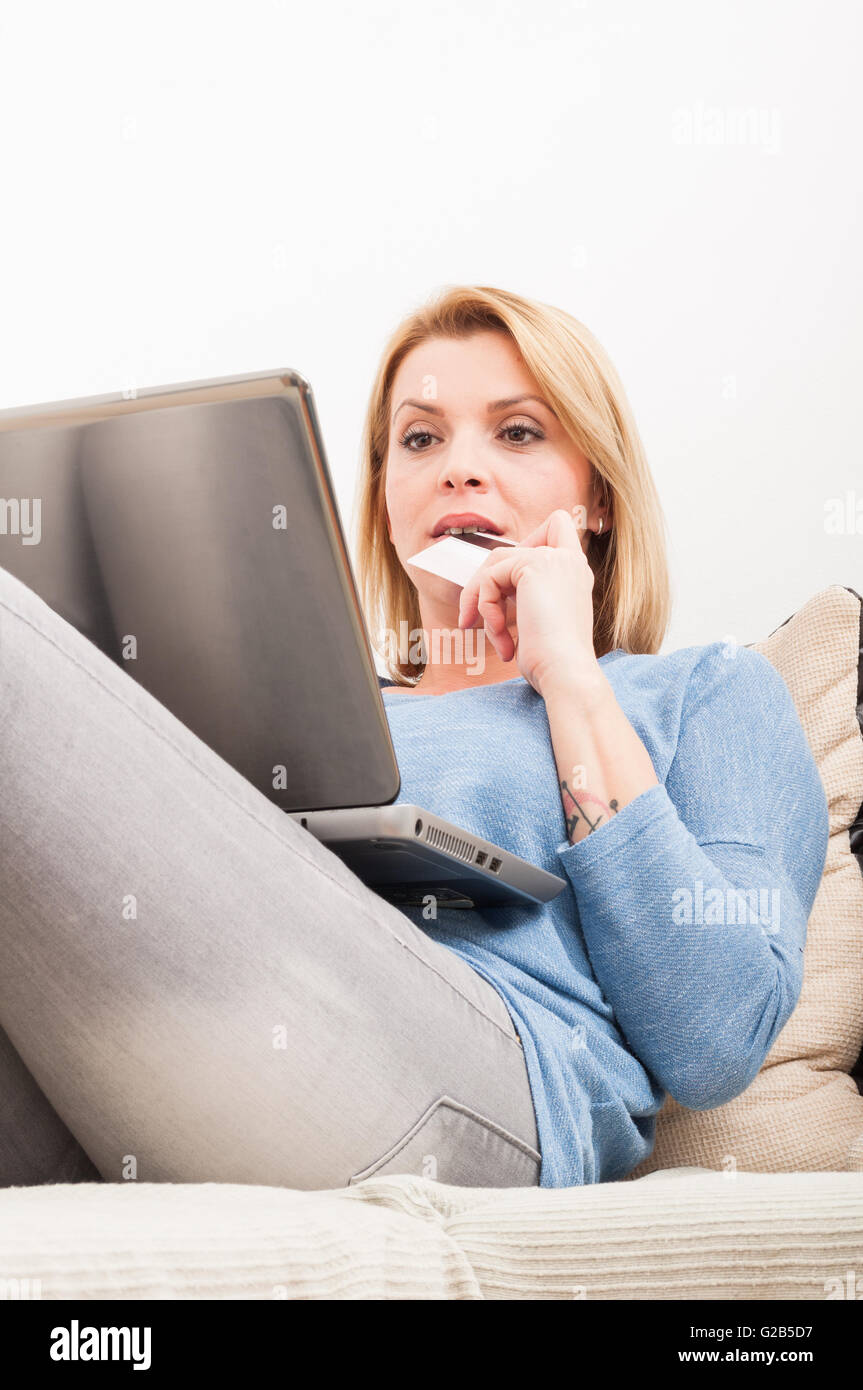 Online-Shop aus dem in- und bezahlen mit Kreditkarte-Konzept mit weiblichen Modell auf der Couch mit laptop Stockfoto