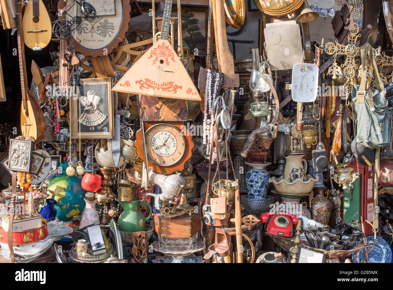 Second-Hand Store Display Dimotiki Agora Athen Griechenland // ATHEN, Griechenland — Ein allgemeiner Second-Hand-Shop in der Nähe der Dimotiki Agora zeigt eine vielfältige Sammlung von gebrauchten und neuen Gegenständen, darunter Uhren, Töpferwaren, Wandkunst, Musikinstrumente und Werkzeuge. Diese Art von vielseitigem Geschäft trägt zum Charakter des zentralen Marktviertels von Athen bei und bietet einen Kontrast zu den frischen Imbissständen der nahe gelegenen Varvakios Agora. Stockfoto