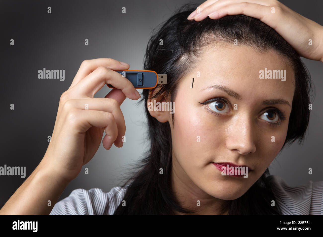 Close-up Schuss in den Kopf eine Business-Frau hält einen Memory-Stick, stecken Sie es in die Seite des Kopfes, erschossen auf einem grauen Hinterg Stockfoto