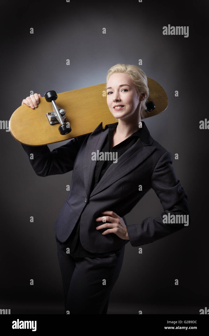 Studioaufnahme von einer Business-Frau mit einem hölzernen Skateboard hautnah.  Schuss auf grauem Hintergrund. Stockfoto