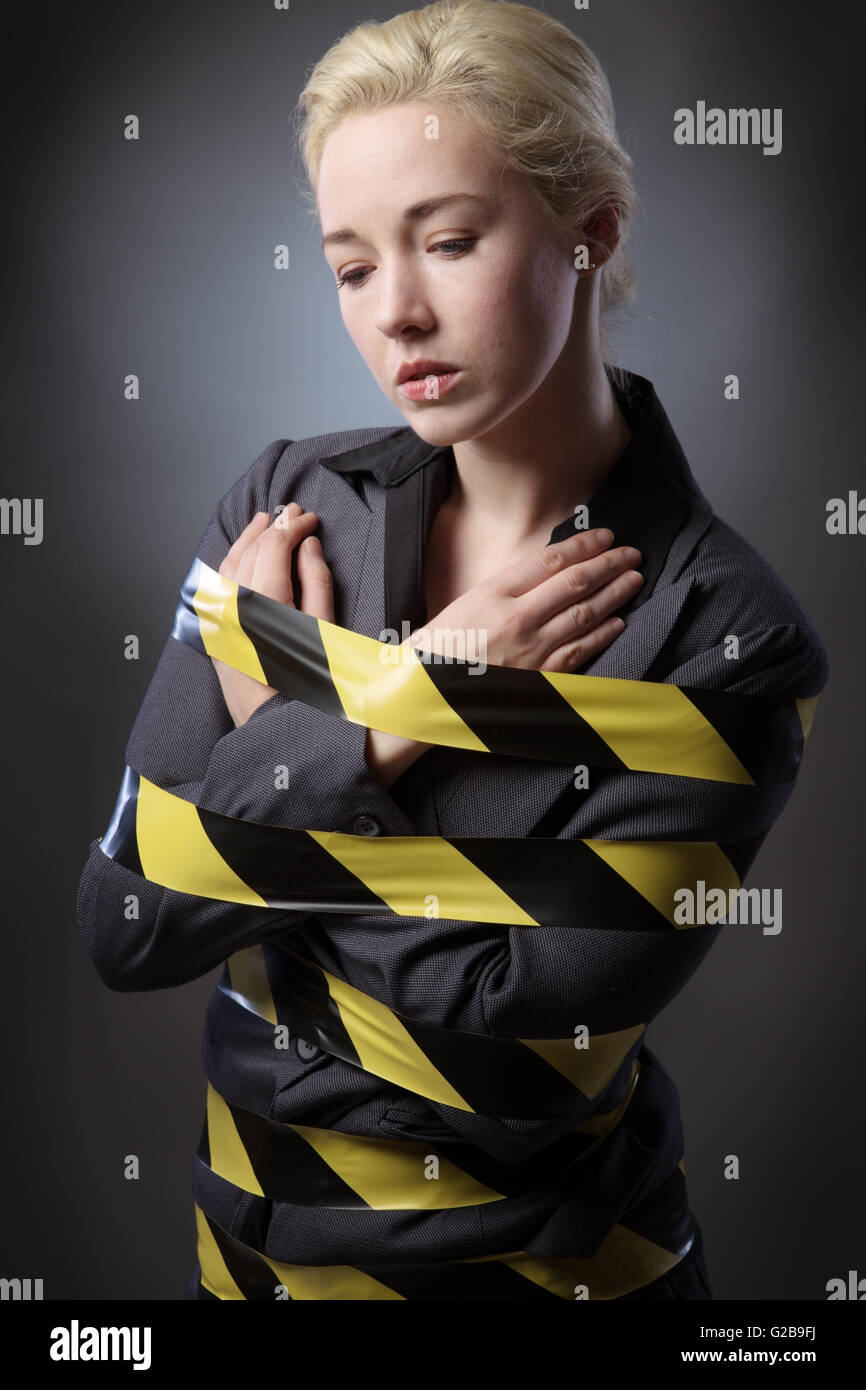 Business-Frau eingewickelt in gelben und schwarzen Band, erschossen auf einem grauen Hintergrund. Stockfoto