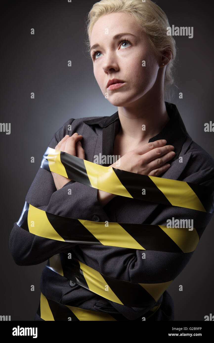 Business-Frau eingewickelt in gelben und schwarzen Band, erschossen auf einem grauen Hintergrund. Stockfoto