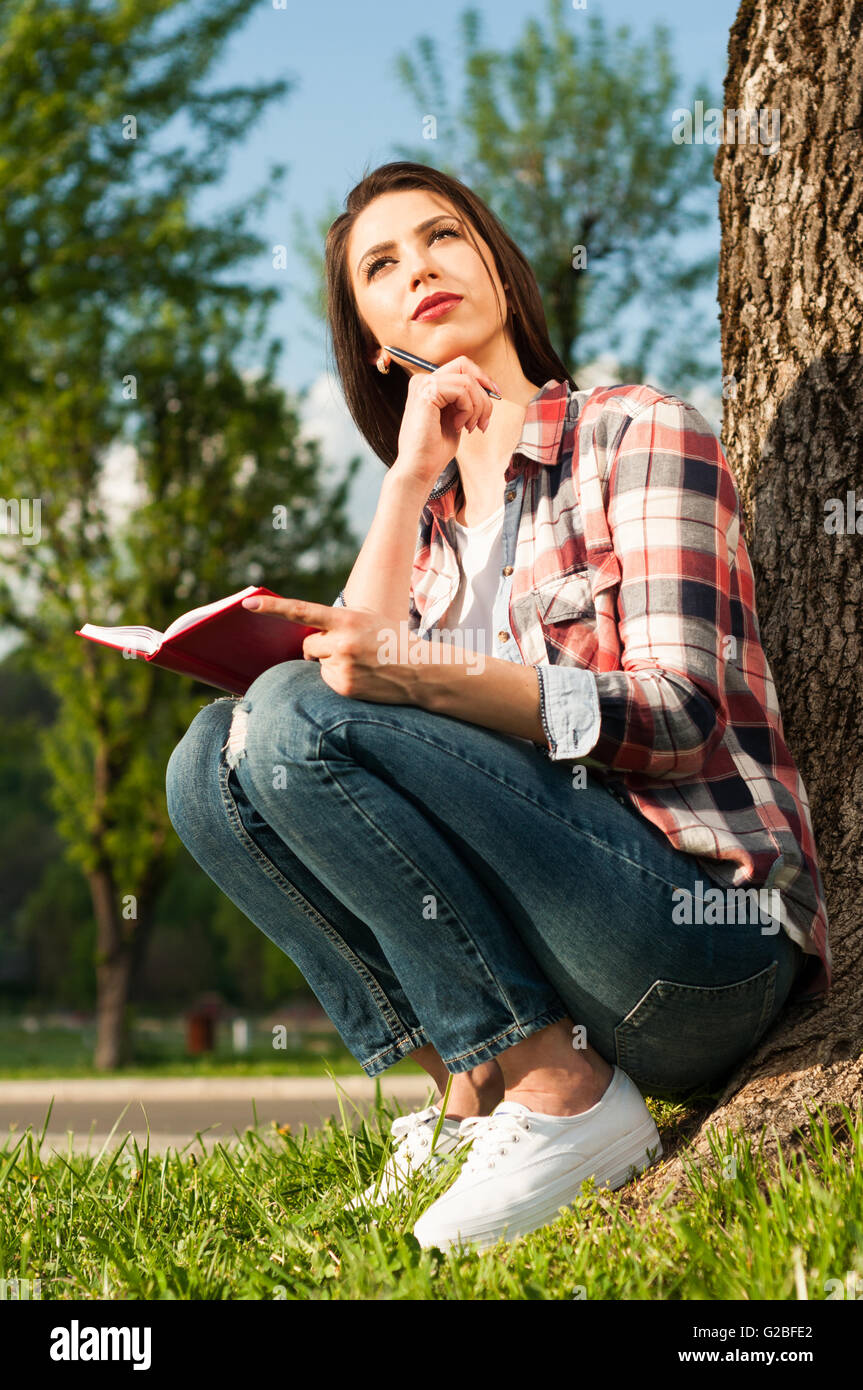 Attraktive nachdenklich weiblichen sitzen Outdor mit Tagebuch neben einem alten Baum im park Stockfoto