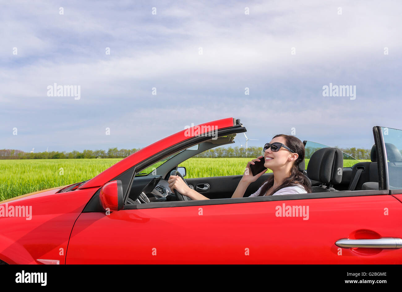 Frau fährt das Auto auf der Landstraße und bei guter Laune am Telefon sprechen. Stockfoto