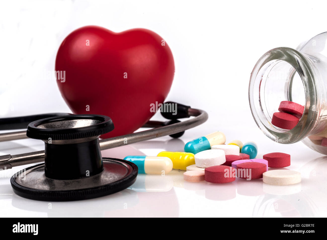 Farbige Tabletten in einem Glas mit rotem Herz und schwarz Stethoskop Stockfoto