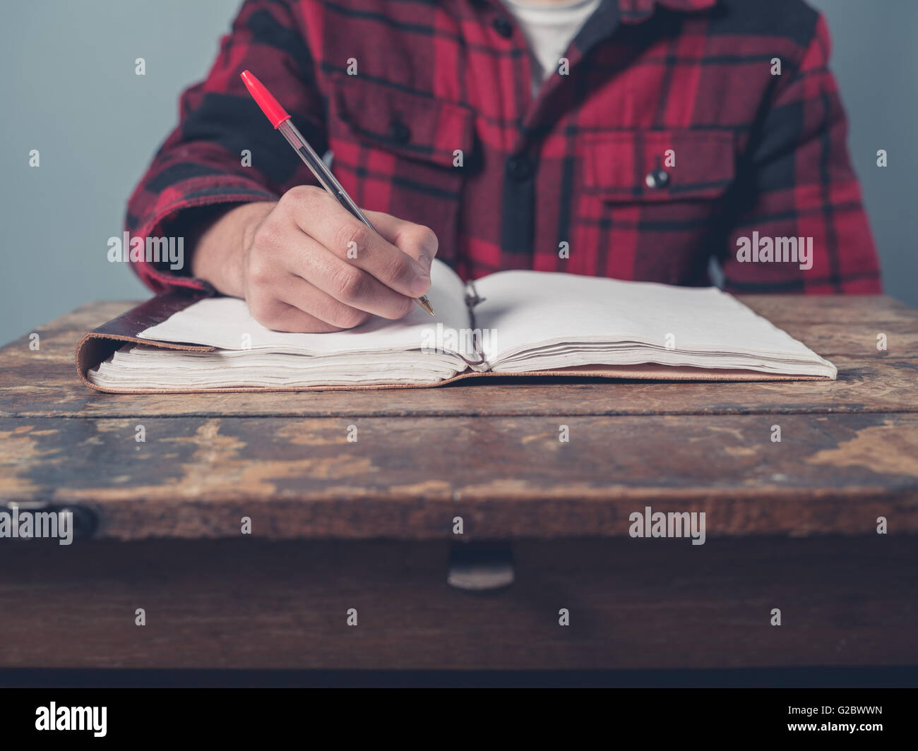 Ein junger Mann mit einer karierten Jacke ist an einem Schreibtisch Notizen. Stockfoto