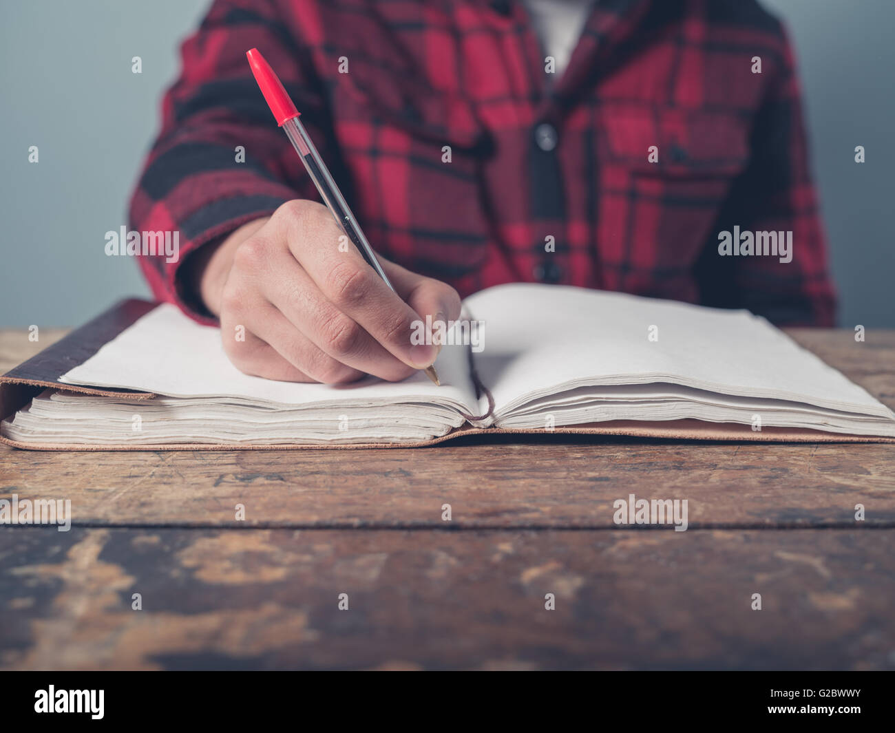 Ein junger Mann mit einer karierten Jacke ist an einem Schreibtisch Notizen. Stockfoto