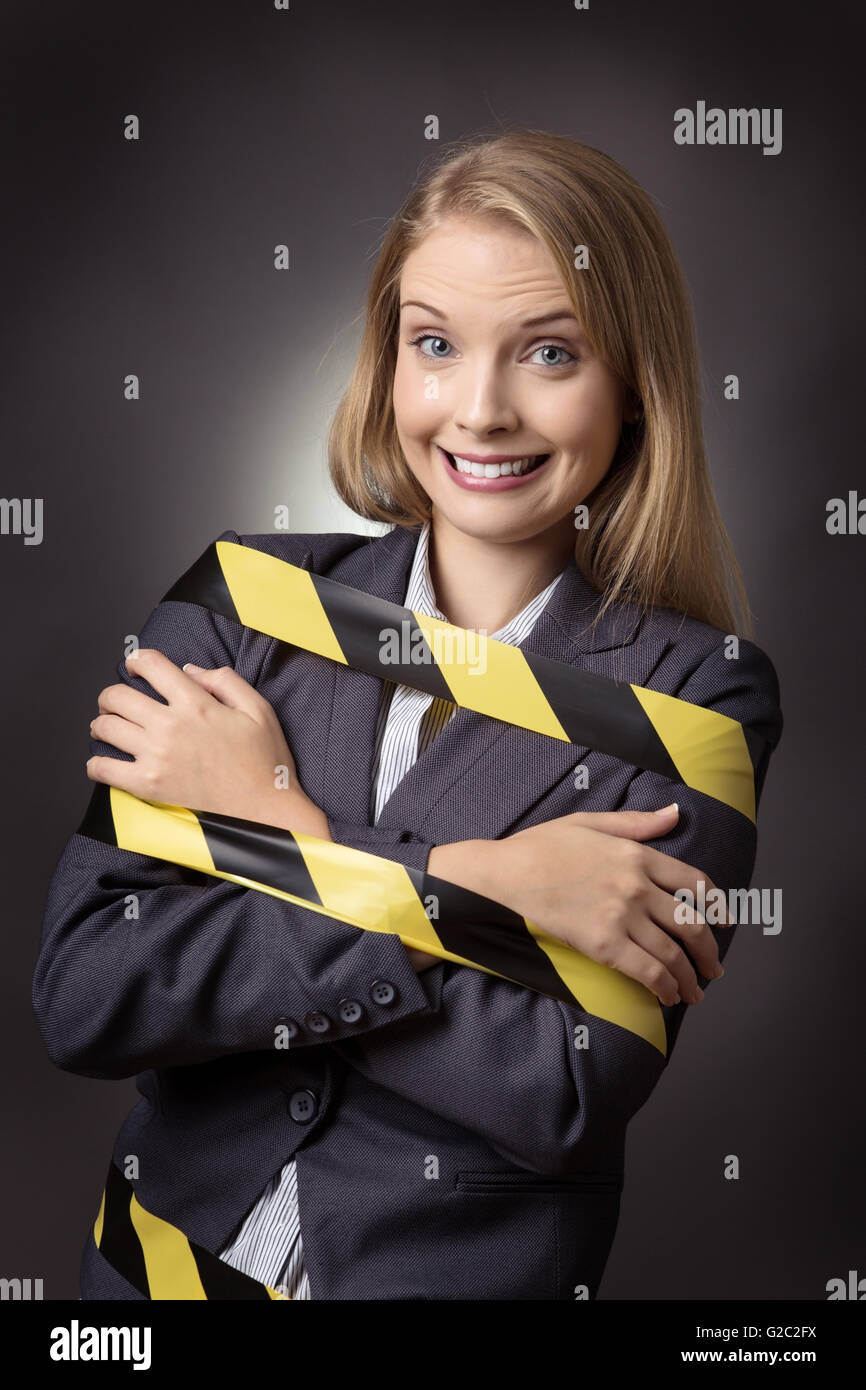 Business-Modell ist mit einem schwarzen und gelben Streifen Klebeband umwickelt ihr gefesselt. Schuss auf grauem Hintergrund. Stockfoto