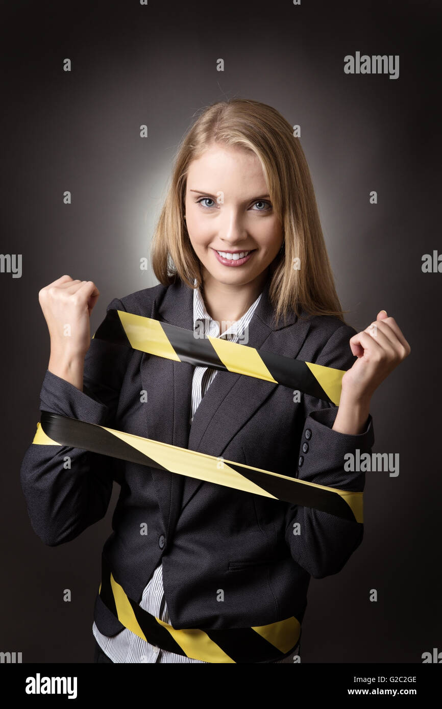 Business-Modell ist mit einem schwarzen und gelben Streifen Klebeband umwickelt ihr gefesselt. Schuss auf grauem Hintergrund. Stockfoto