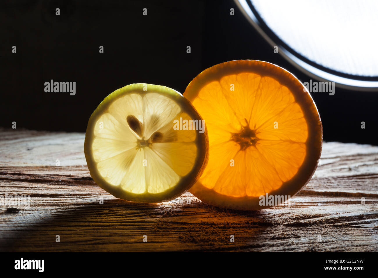 Scheiben von Orange und Zitrone mit durchscheinenden Licht mit Lichtquelle im Hintergrund auf rauen Holzoberfläche Glühen Stockfoto