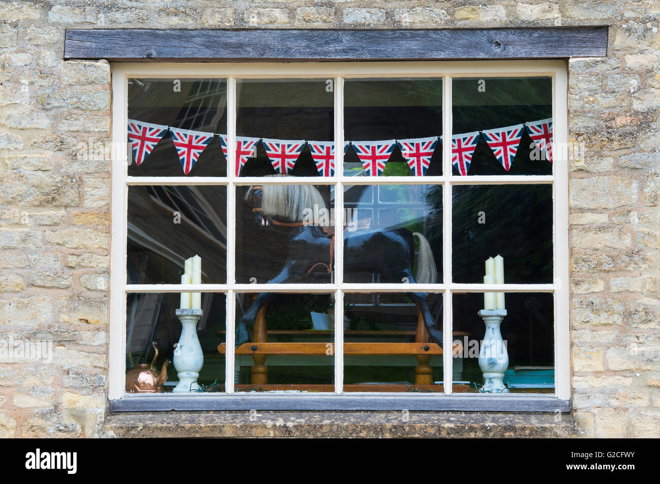 Rocking Horse und Union Jack Bunting in das Fenster von The Old Post Office Shop, Guiting Power, Gloucestershire, England Stockfoto