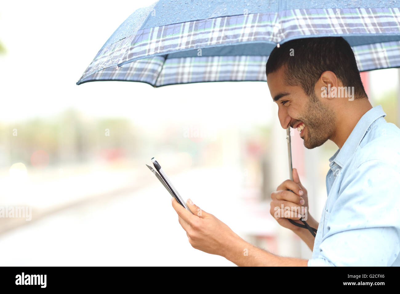 Profil eines muslimischen Mannes lesen eine Tablette unter einem Sonnenschirm an einem regnerischen Tag Stockfoto