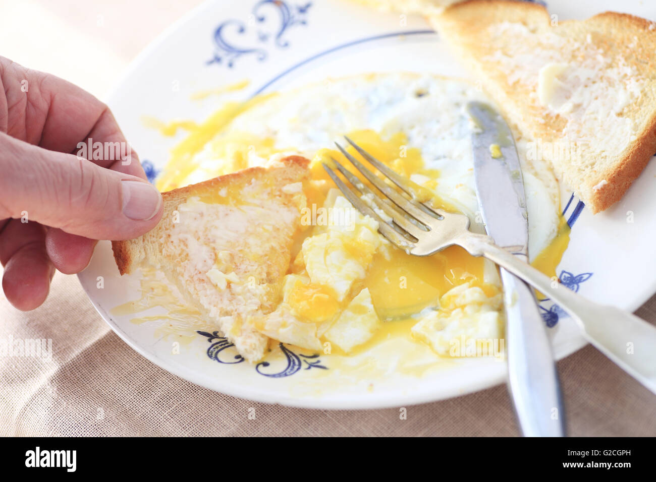 Ein Mann isst laufende Spiegeleier mit Hilfe von einem Stück Butter Toast zum Frühstück. Stockfoto