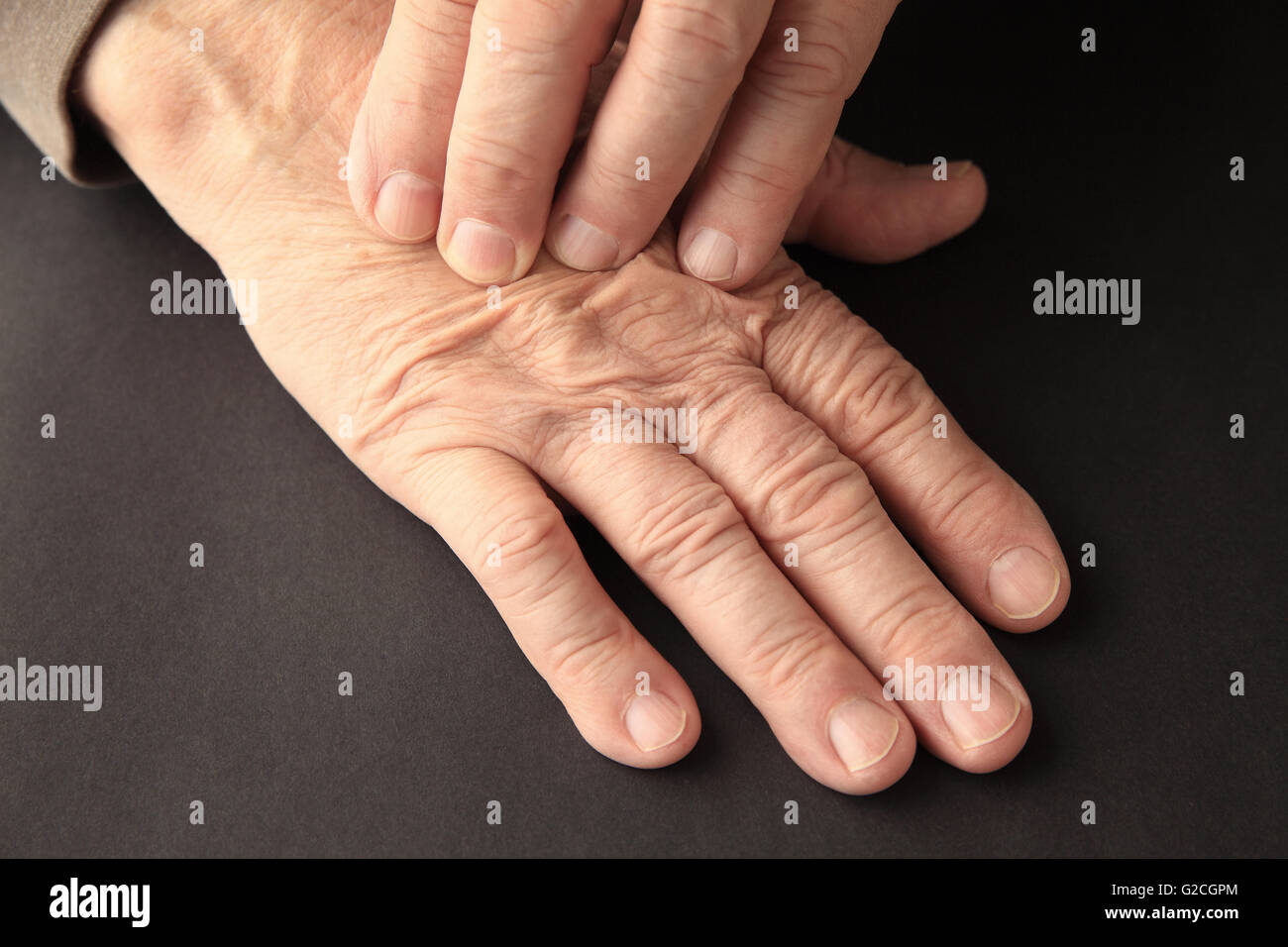 Ein älterer Mann hat Schmerzen an seiner Hand auf einem schwarzen Hintergrund. Stockfoto