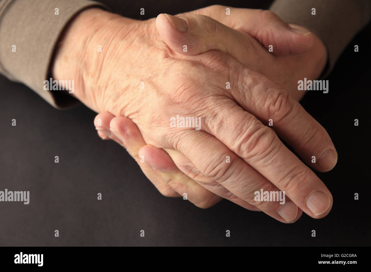Ein älterer Mann ergreift seine Hand auf einem schwarzen Hintergrund mit Textfreiraum. Stockfoto