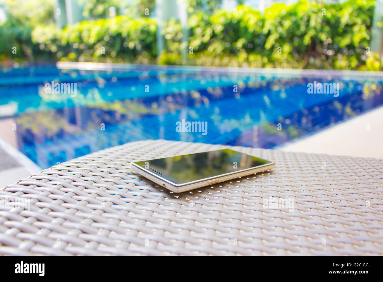 Smartphone auf Sessel neben dem Pool setzen bedeutet, vom Geschäft ruht bekommen Stockfoto