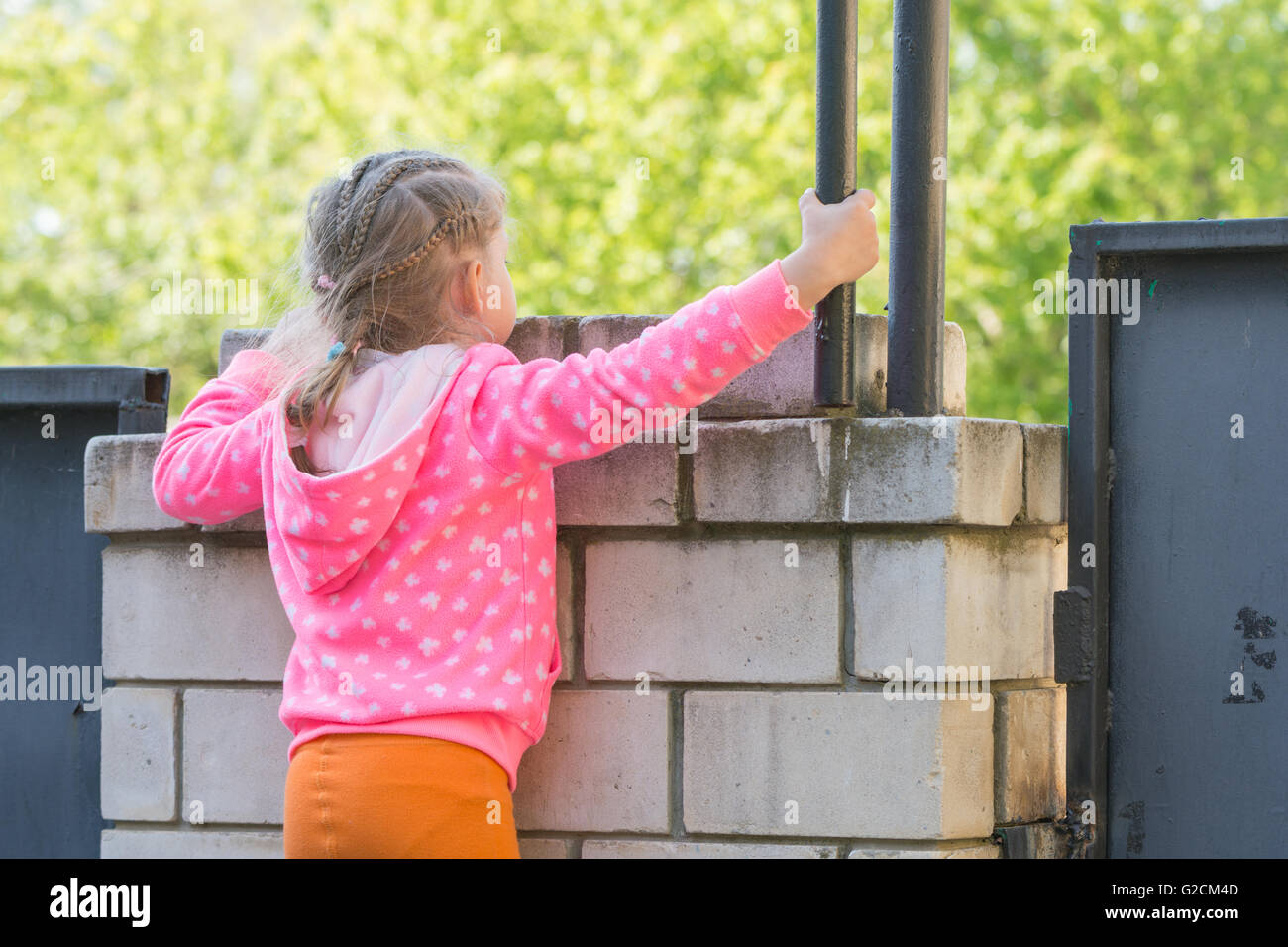 Fünfjähriges Mädchen kletterte auf eine Ziegelmauer und sieht für ihn Stockfoto