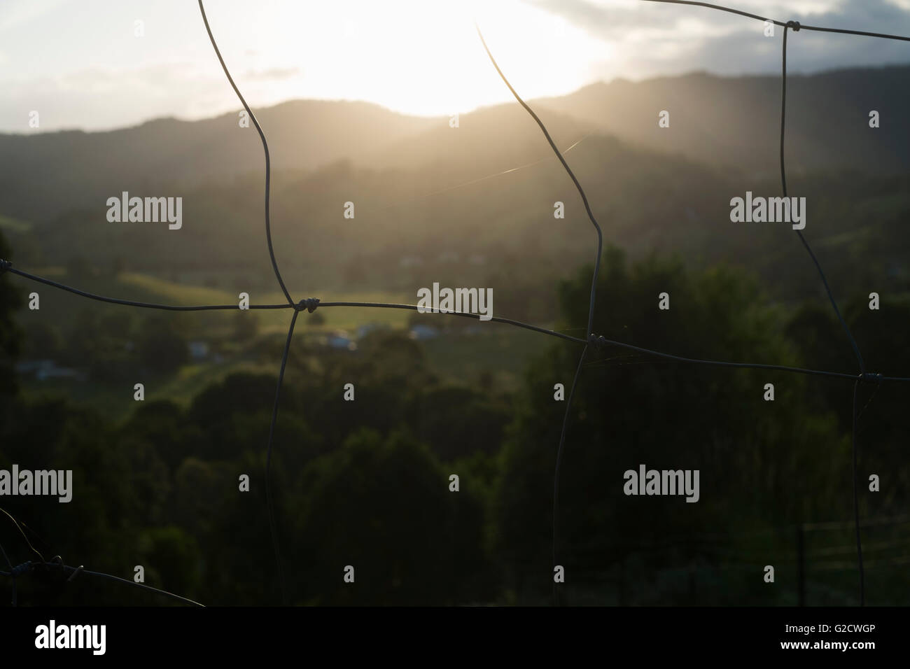 Der Blick durch den Zaun der Farm von Heizer Abstellgleis der Sonnenuntergang hinter den Bergen weit Norden New South Wales. Stockfoto