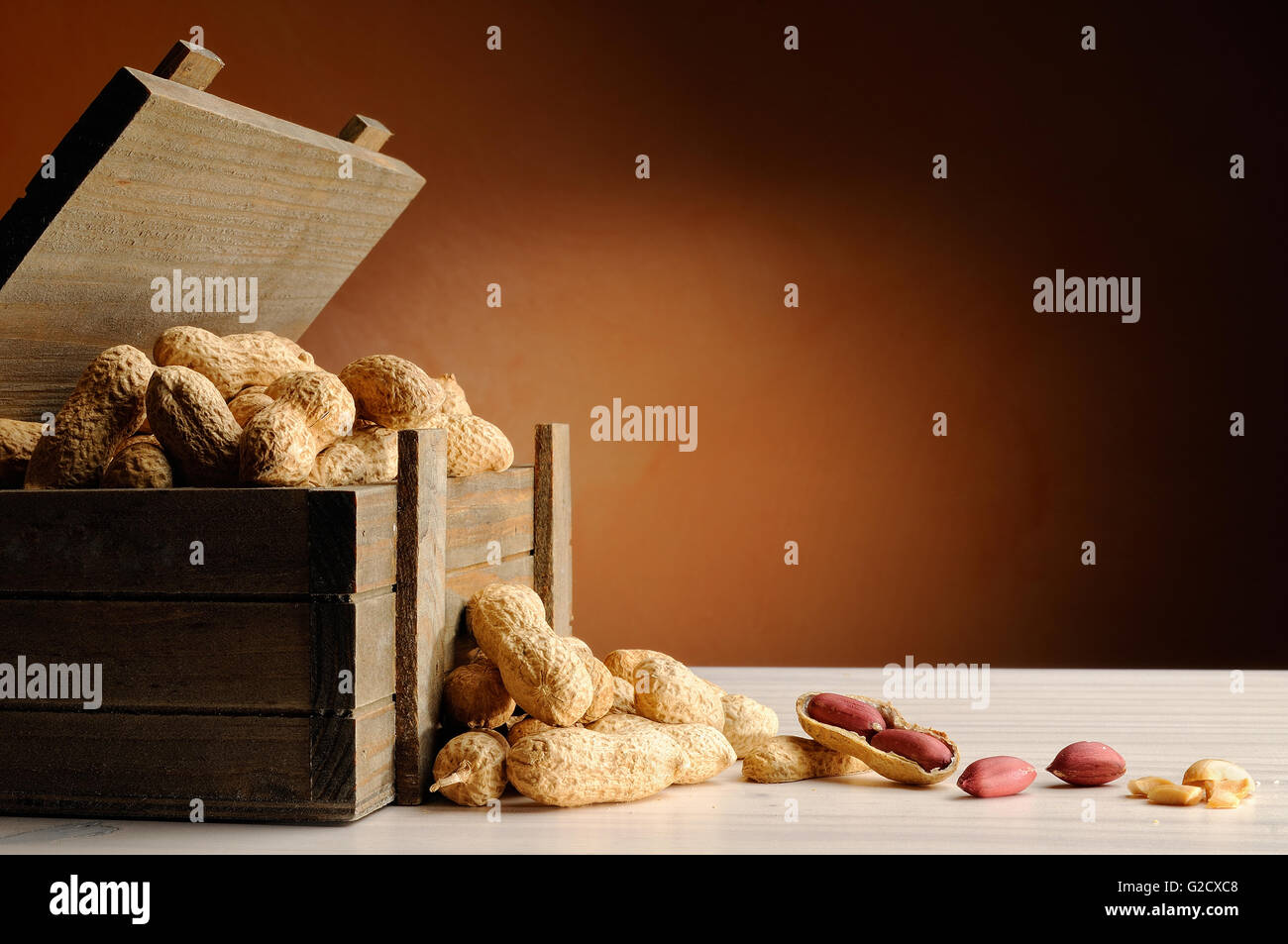 Gruppe von Erdnüssen auf einem weißen Tisch mit Stamm Holzcontainer und braunen Hintergrund Stockfoto