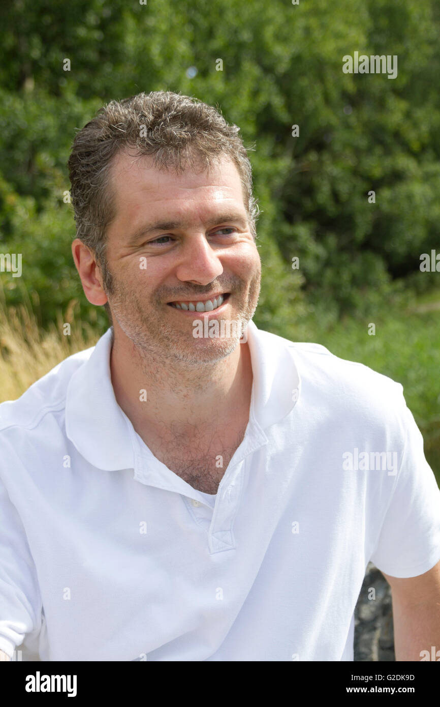 45 - Jahre alter Mann mit Stoppeln lächelnd an einem sonnigen Sommertag im Urlaub in der Natur Stockfoto