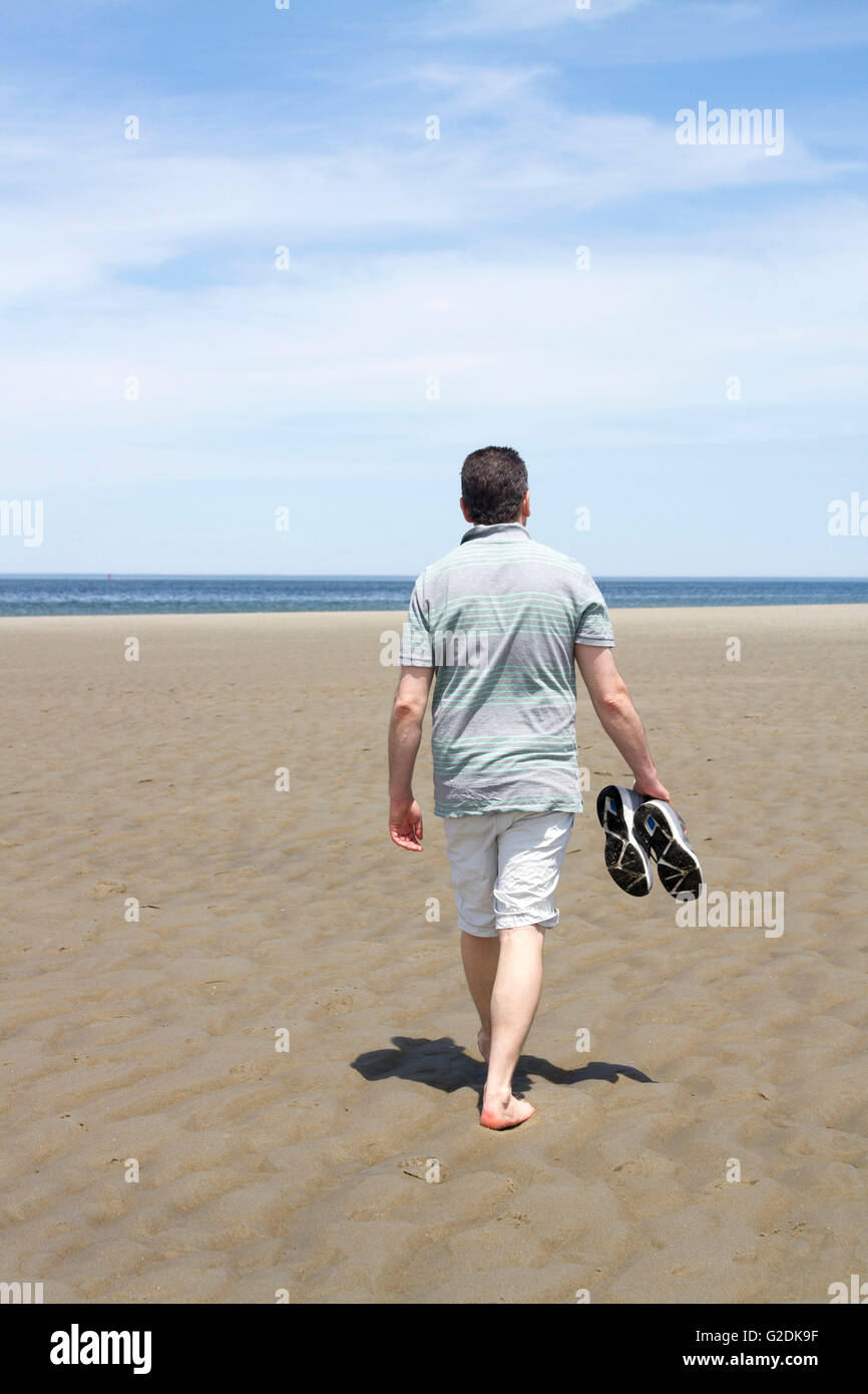 Mann zu Fuß auf einem Sandstrand seine Schuhe tragen Stockfoto