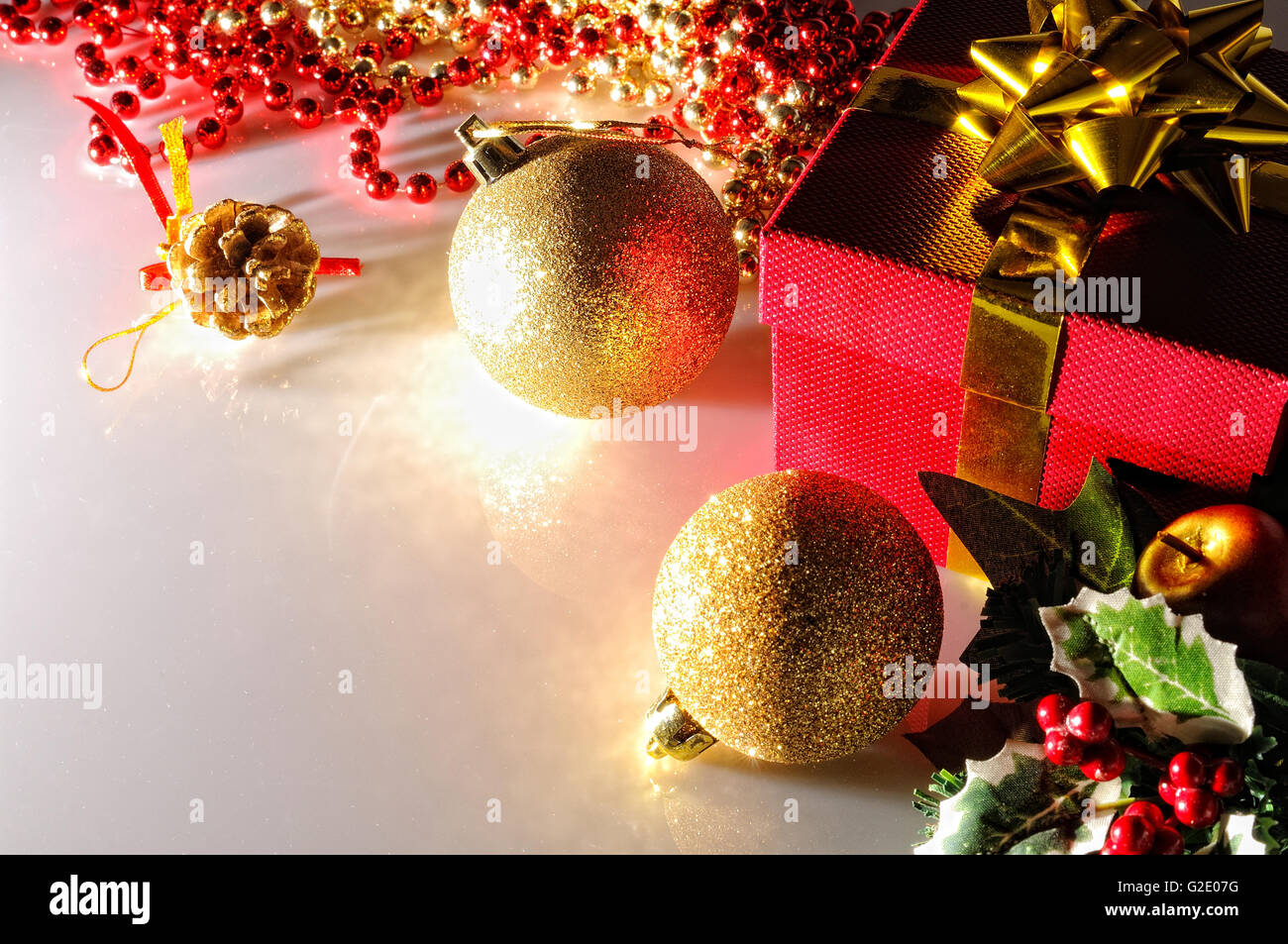 Düsternis Weihnachtsdekoration auf einem weißen Methacrylat-Tisch. Roten Geschenkbox mit Goldband, zwei Goldene Kugeln und Perlen. Ansicht von oben. Stockfoto