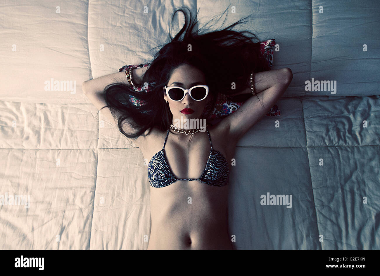 Junge Frau mit Sonnenbrille und Bikini Top mit auf Bett, High Angle View Stockfoto