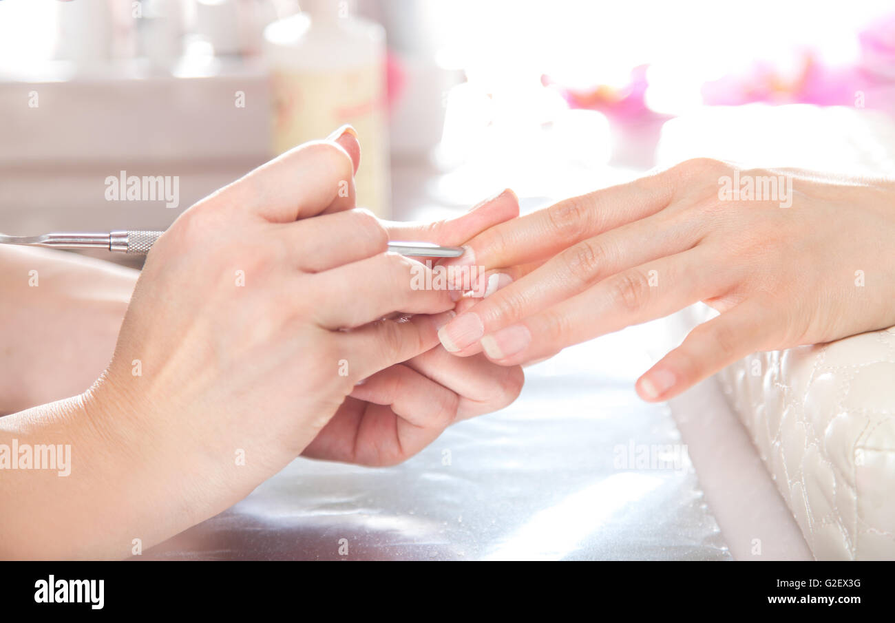 Maniküre Pediküre Nagelstudio. Kosmetikerin tut Nagelhaut Pflege mit Nagelhautschieber für den Kunden. Stockfoto