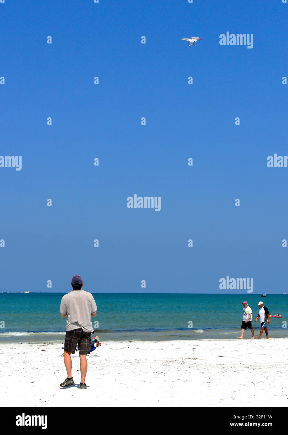 Eine zivile Drohne fliegt über Kopf am Strand mit einem Rückansicht des Piloten suchen den Himmel an einem sonnigen Tag mit blauem Himmel Stockfoto