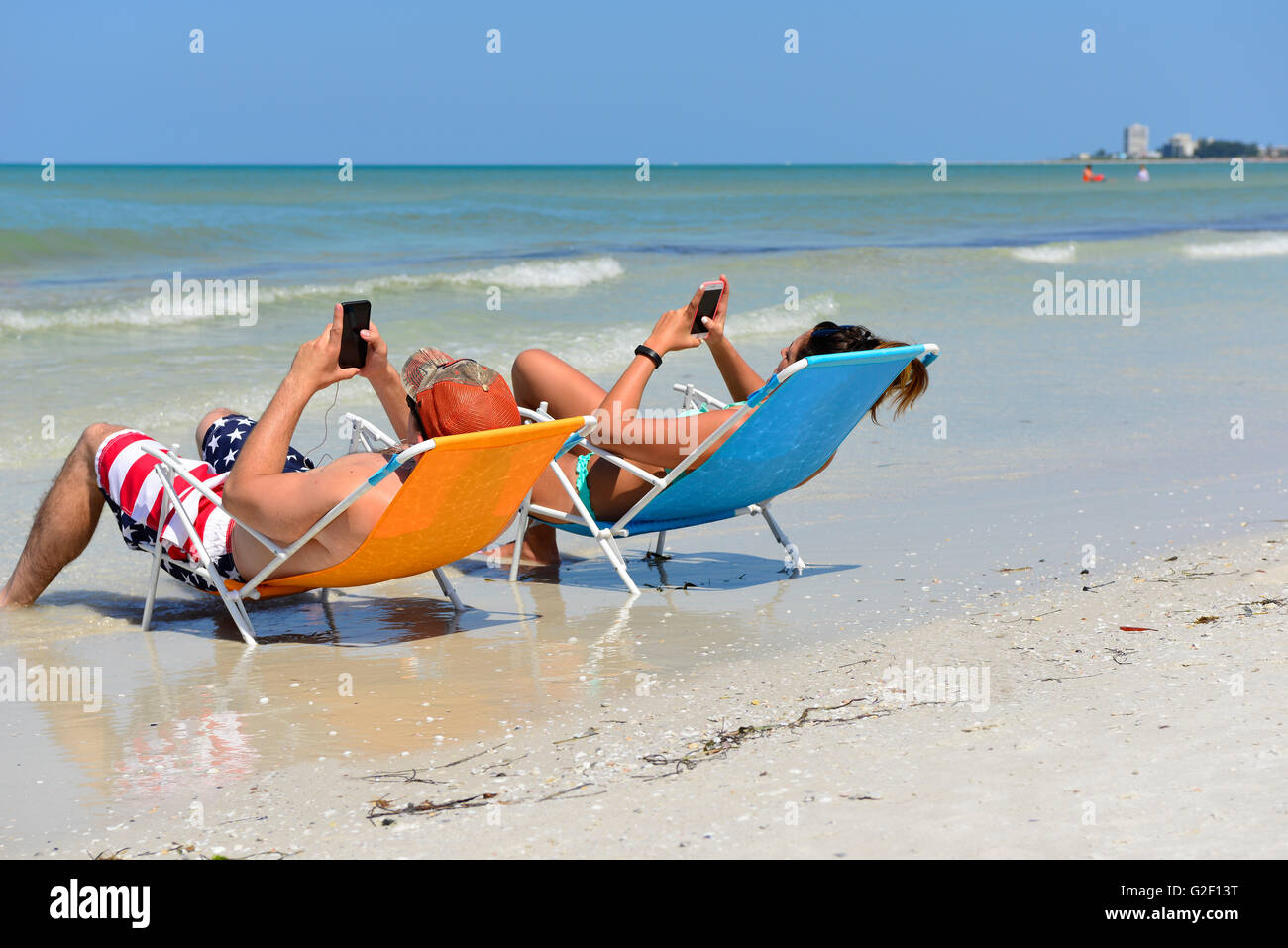 Beschäftigt paar kann nicht aufhören, ihre Handys zu einander oder der Strand Küste genießen, während in den Stühlen liegen Stockfoto