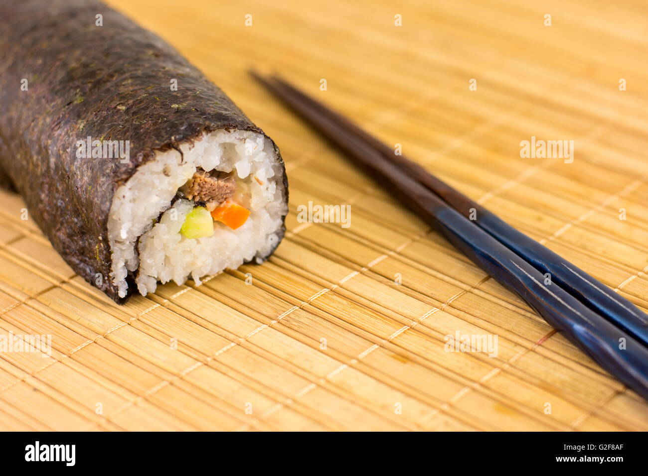 Sushi-Rolle und Stäbchen auf Bambus-Tischdecke Stockfoto