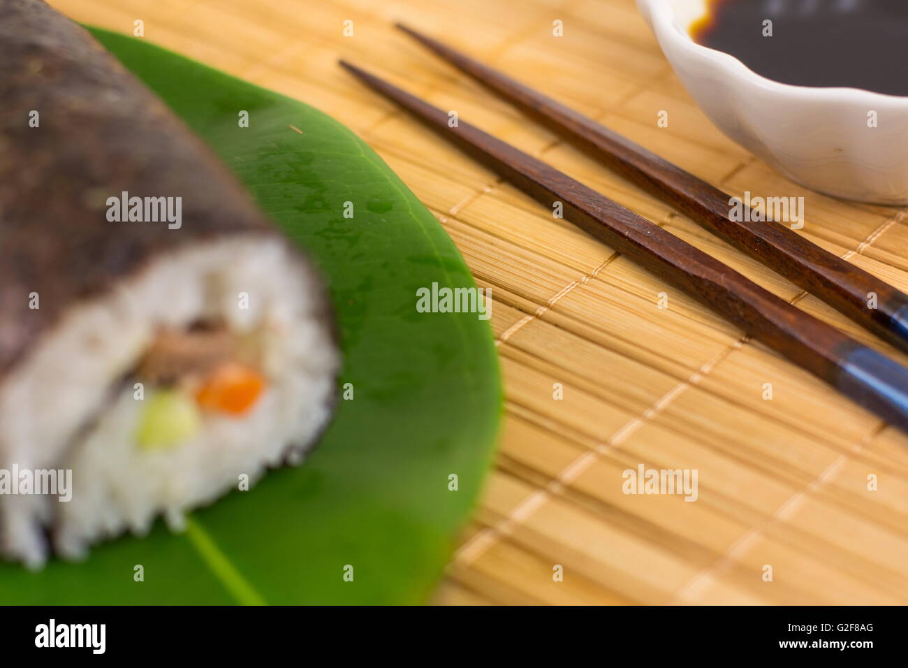 Sushi-Rolle und Stäbchen auf Bambus-Tischdecke Stockfoto