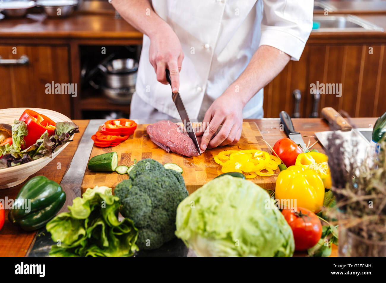 Profi-Koch Kochen stehen und Schneiden von rohem Fleisch und frisches Gemüse  in der Küche Stockfotografie - Alamy