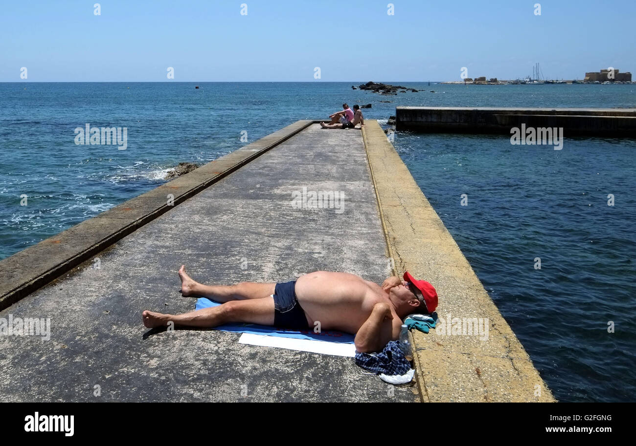 Ein Mann liegt allein, Sonnenbaden neben dem Meerwasser-Schwimmbad auf der Paphos, direkt am Meer, Zypern, Stockfoto