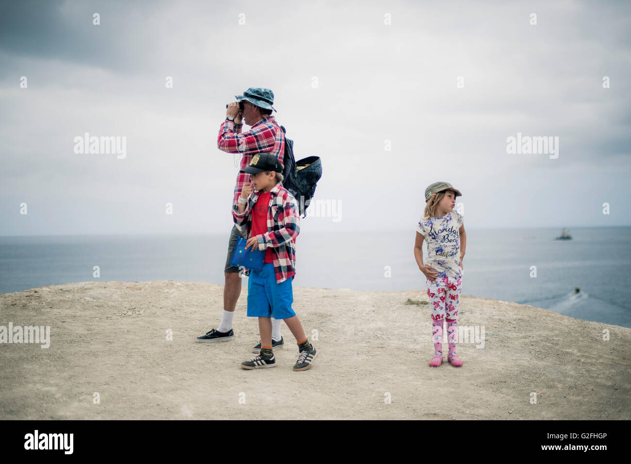 Vater durch ein Fernglas während mit zwei Kindern auf küstennahen Klippen Stockfoto