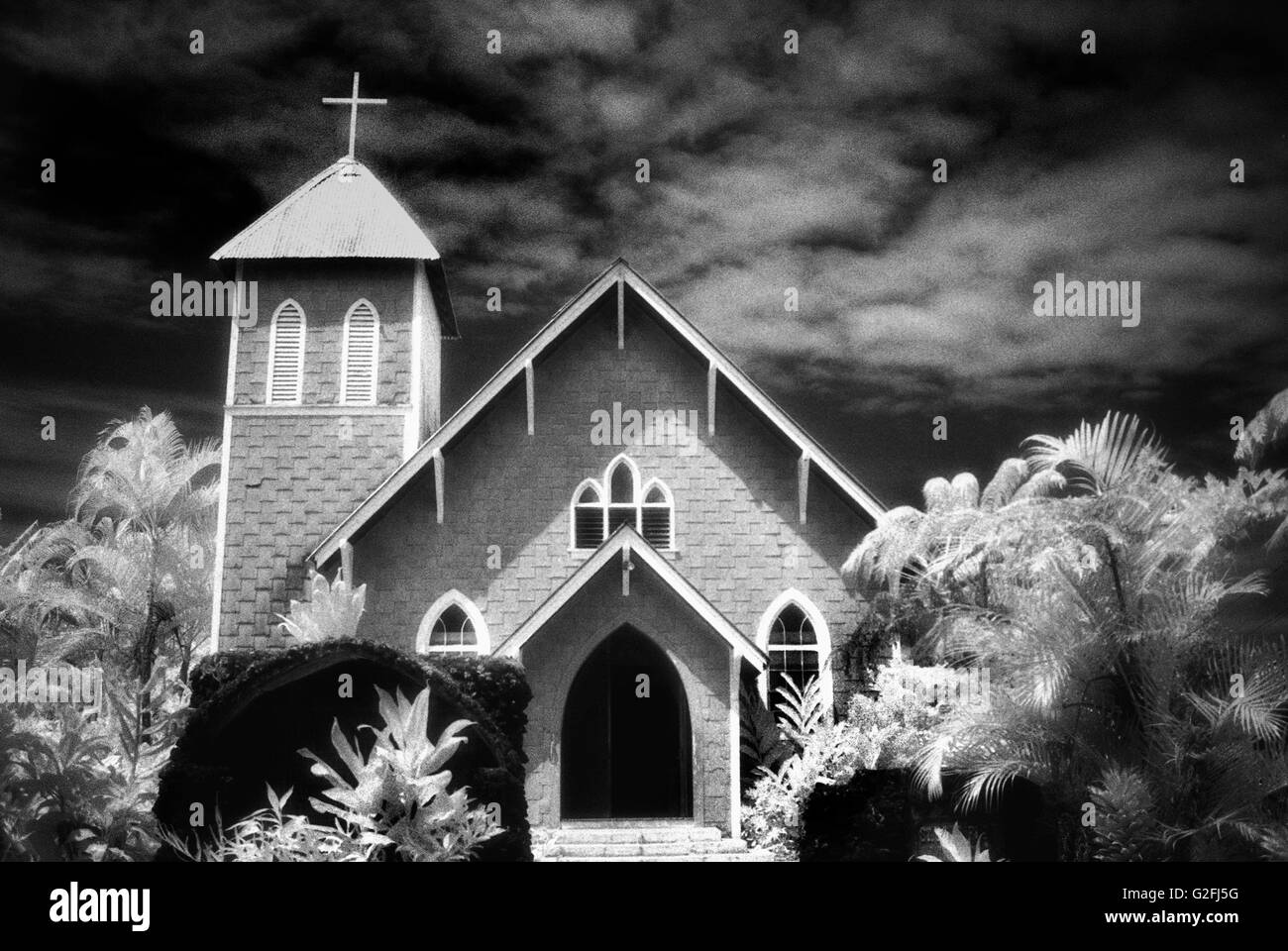 Malerische Kirche mit Kreuz am Turm in tropischer Umgebung vor dramatischen Himmel, Maui, Hawaii, USA Stockfoto
