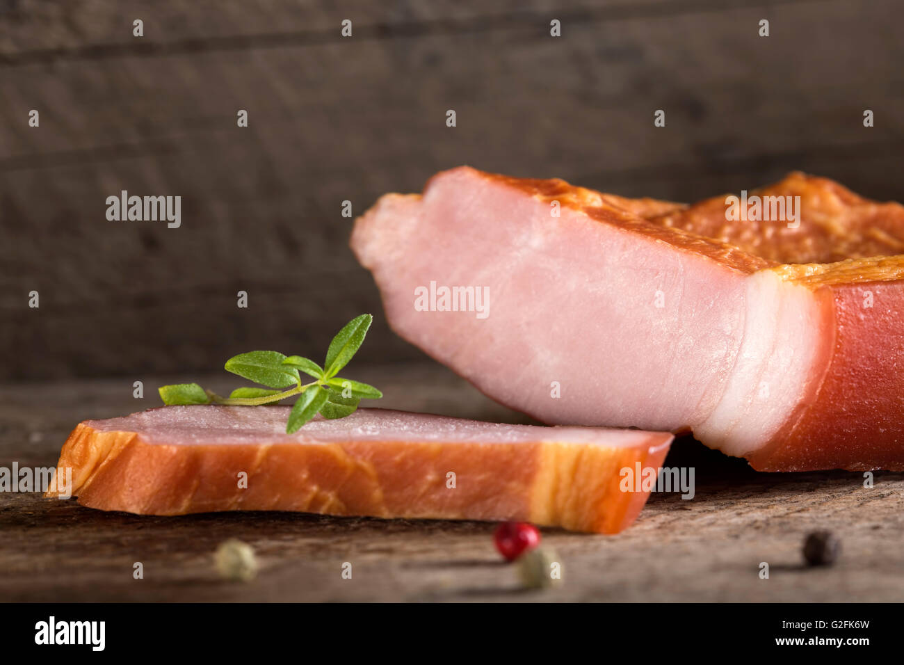 Nahaufnahme von geräuchertem Schweinefleisch Filet Scheiben auf Holztisch mit Kräutern Stockfoto