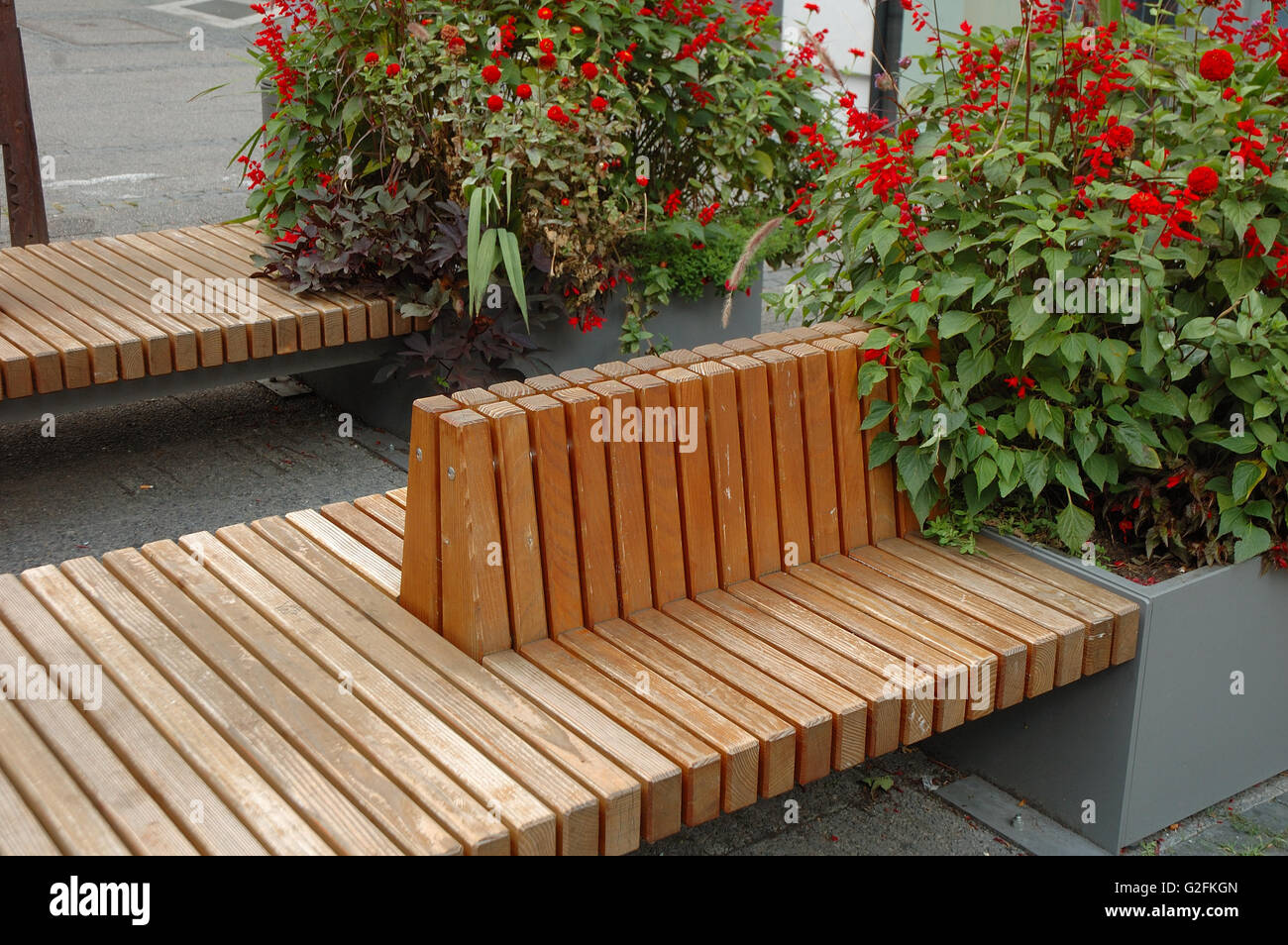 Zwei braune Holzbänken und rote Blumen auf Straße. Stockfoto