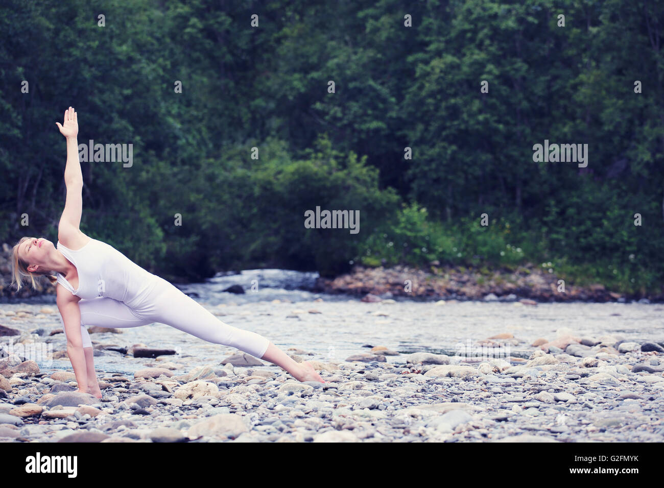 Junge Frau übt Yoga am Stein Ufer Fluss Stockfoto