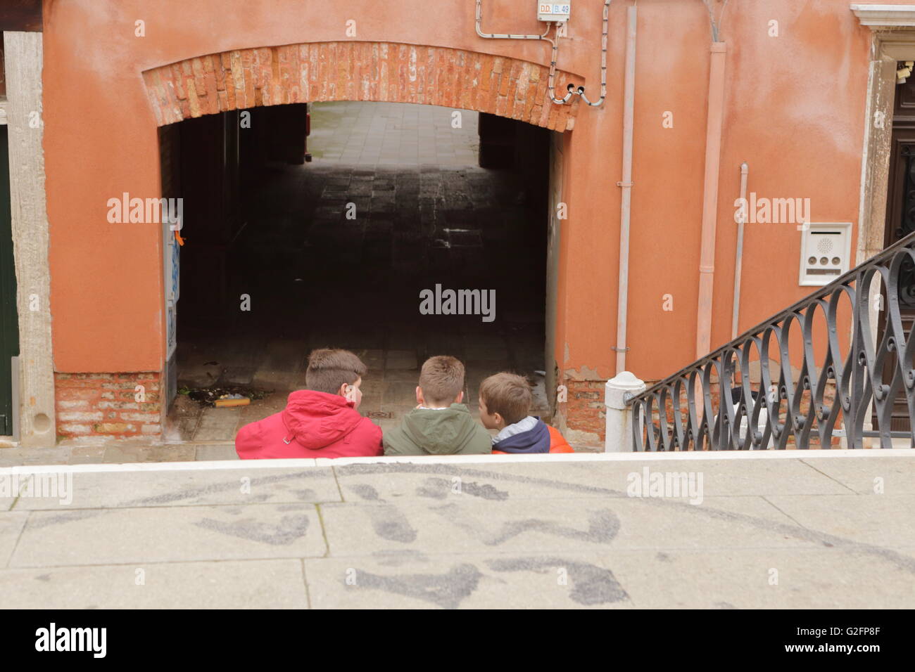 Drei Kinder sitzen auf den Stufen einer Brücke über einen Kanal in Venedig, Italien Stockfoto