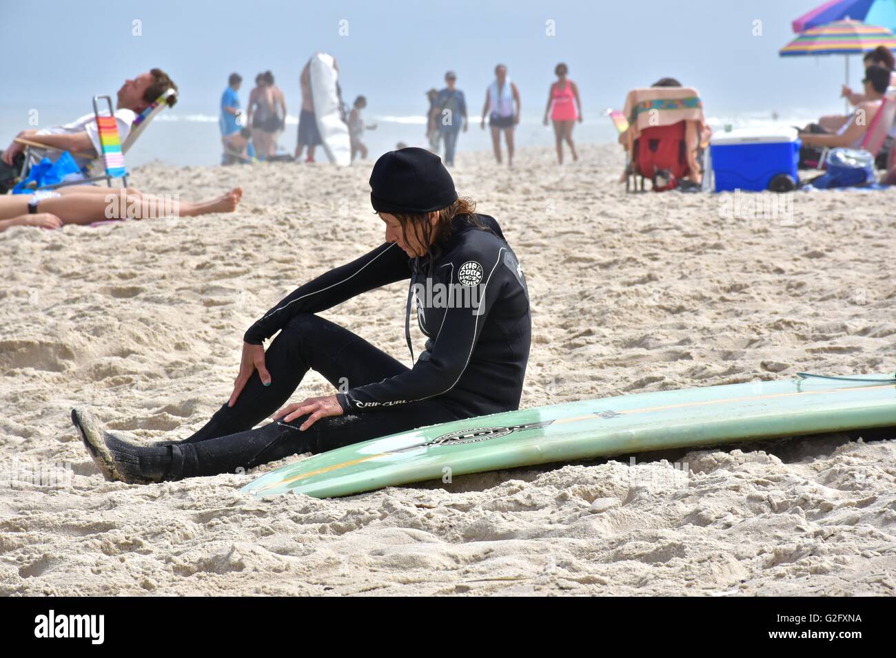 Eine Frau in einem Neoprenanzug sitzt am Strand neben ihrem Surfbrett Stockfoto