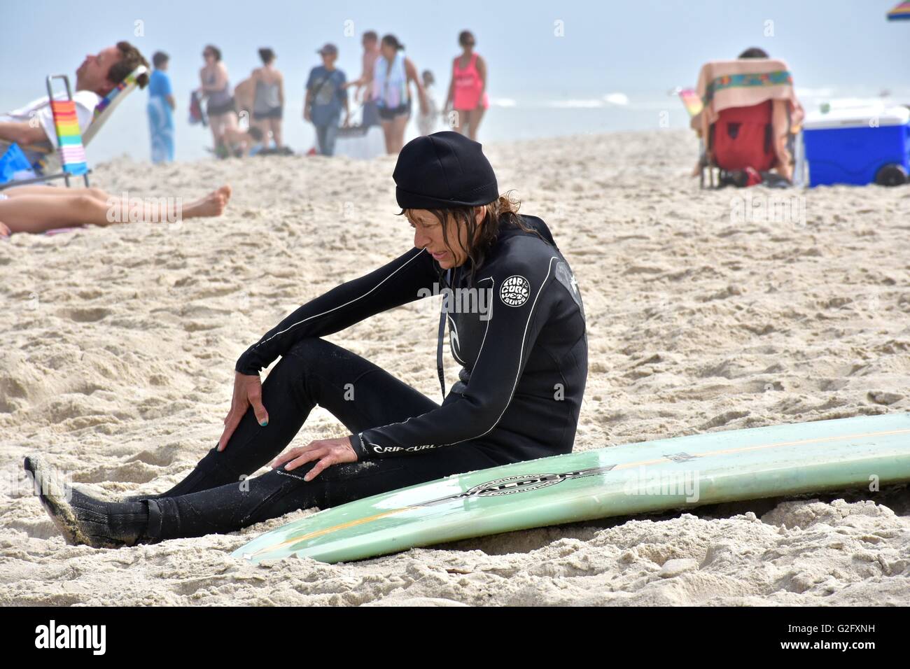 Eine Frau in einem Neoprenanzug sitzt am Strand neben ihrem Surfbrett Stockfoto