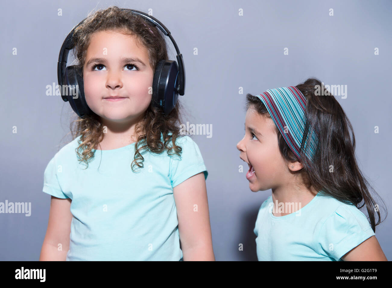 Porträt von kleinen Mädchen schreien an ihrer ältesten Schwester anhören von Musik im Kopfhörer Stockfoto