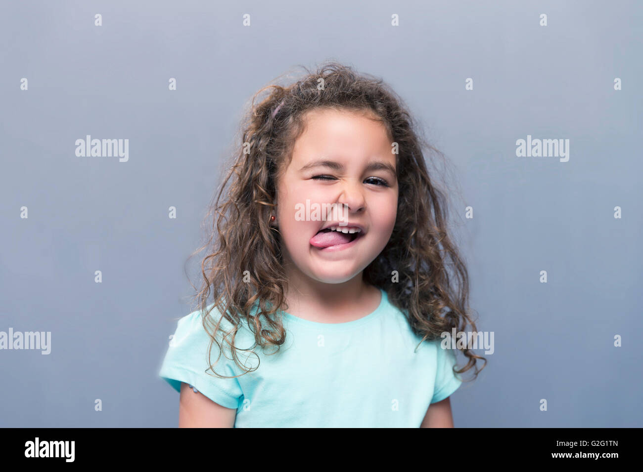 Porträt der niedliche lockige Mädchen zeigen Zunge und Augen Schielen. Isoliert Stockfoto