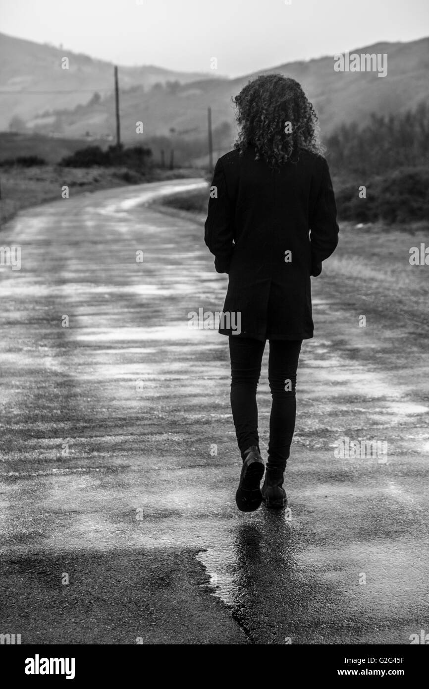 Junger Mann mit lockigem Haar Walking Down Road, Rückansicht Stockfoto