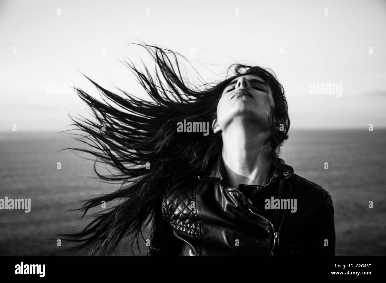 Young Adult Woman Portrait mit Kopf in den Nacken und langes Haar weht im Wind mit Meer im Hintergrund Stockfoto