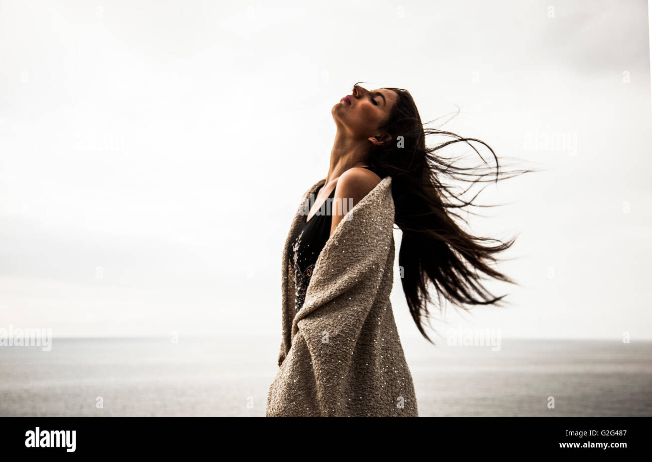 Young Adult Woman Portrait mit Kopf in den Nacken und langes Haar weht im Wind mit Meer im Hintergrund Stockfoto